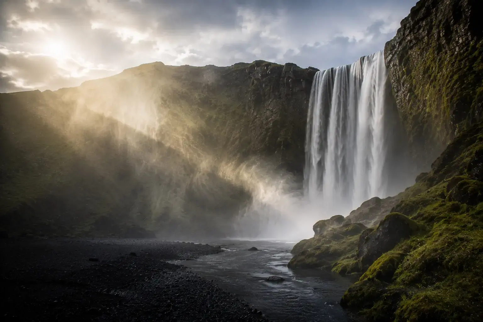 Adventure Quest artwork from the Iceland collection: a tall waterfall pouring past dark cliffs through mist and low sunlight.